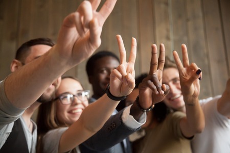 Close up of smiling multiracial people showing V sign making group picture, spending time, having fun together, happy diverse students gesturing victory or peace symbol demonstrating racial equalityの写真素材