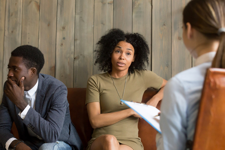 Black millennial couple visiting therapist office, upset African American wife discussing marriage problems and complaints with psychologist during session with husband. Family counsel conceptの写真素材