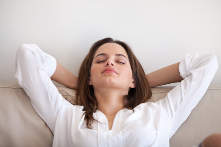 Relaxed woman lying eyes closed hands over head on cozy sofa at home, calm millennial female sleeping or taking nap during lazy morning, spending weekend in apartment, girl chilling or taking breakの写真素材