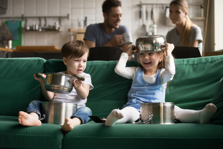 Happy funny cute little boy and girl playing with kitchenware cooking pots at home, preschool kids sister and brother laughing holding kitchen utensils, children son and daughter having fun togetherの写真素材