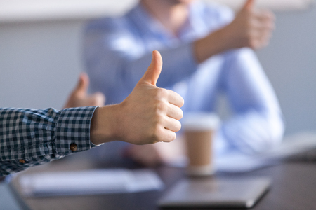 Close up of thumb up shown by male worker during office meeting, celebrating good deal or company success, worker make like gesture motivated by productive teamwork or goal achievementの写真素材