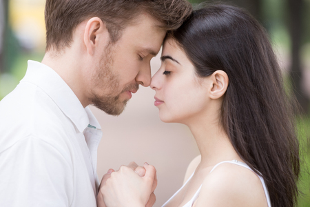 Close up of sensual young couple holding hands touching noses enjoying romantic moment together outdoors, tender boyfriend and girlfriend standing eyes closed feeling intimacy and closenessの写真素材