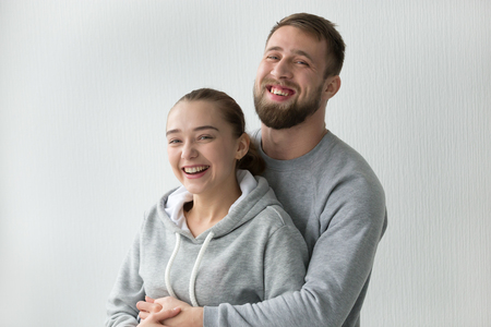 Portrait of smiling millennial couple looking at camera hugging laughing, boyfriend and girlfriend embracing in newly bought own apartment, happy man hold excited woman in arms at homeの写真素材