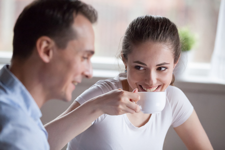 Happy woman smiling spending time with handsome man, cute young girl drinking coffee talking with date or partner, millennial couple enjoy conversation indoors chatting and laughing having funの写真素材