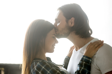 Romantic boyfriend kissing girlfriend in forehead, loving couple enjoying sweet tender moment together, passionate millennial spouses hugging caressing, happy lovers have intimacy in bedroomの写真素材