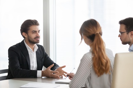 Confident millennial male job applicant talk at interview in office, HR team listen seriously to man...