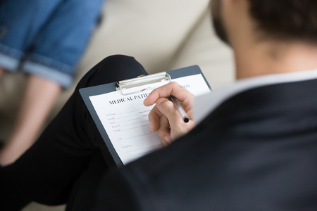 Close up of male psychologist or doctor holding clipboard with medical card listening to patient problems, expert or counselor take notes or fill information during therapy session or counselingの写真素材