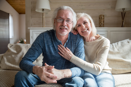 Smiling senior middle aged vloggers couple looking talking at camera recording video blog at home, happy friendly mature old family making videocall sitting on sofa, elderly lifestyle vlog conceptの写真素材