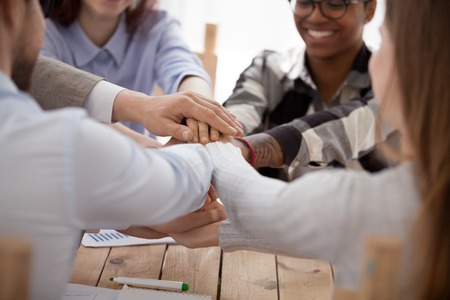 Close up group of young millennial business people or students stacking their hands palm, sitting in...