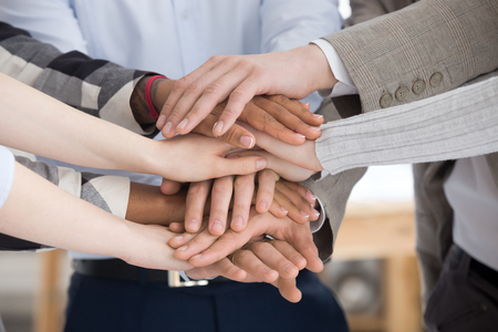 Close up of multiracial group of millennial business people or students standing stacking theirs...