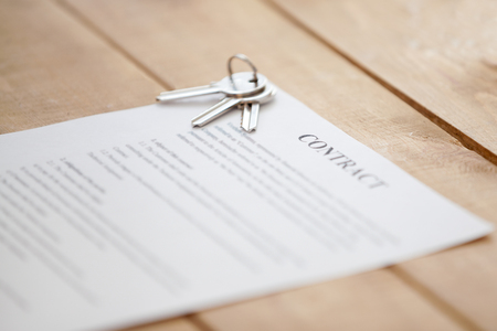 Close up of keys lying on a contract document paper on a wooden table. New dwelling or home successful real estate deal, buying selling, renting and tenancy, mortgage and loan concept, focus on keys