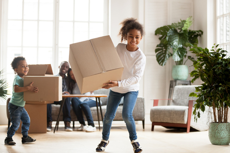 Black family in living room at new home. Happy parents sitting on couch looking at children, preschool daughter toddler son playing carrying cardboard boxes. New house, buying property, moving conceptの写真素材