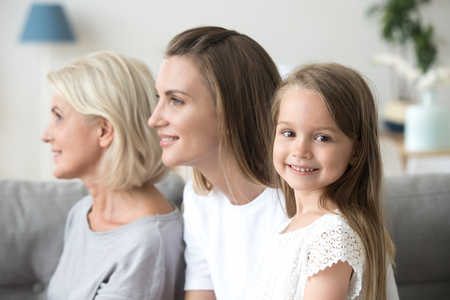 Portrait of cute little girl looking at camera smiling, mother and grandmother watch in distance...