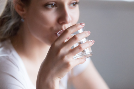 Close up millennial woman holding glass looking away drinking still water, focus on hand. Beautiful...