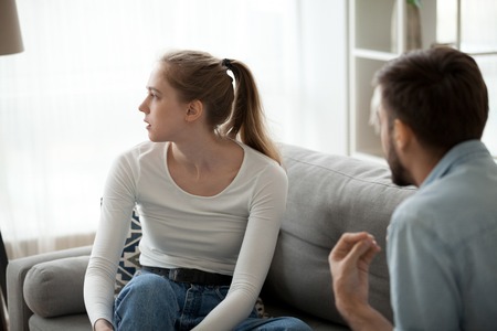 Unhappy couple sitting on couch in living room at home sorting out their relationships quarrelling. Guy arguing emotionally talking frustrated girl looking away. Break up problems in relations conceptの写真素材