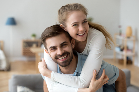 Head shot happy millennial young man and woman hugging embracing indoors. Portrait close up smiling husband and wife piggyback ride looking at camera laughing. Dating and romantic relationship conceptの写真素材