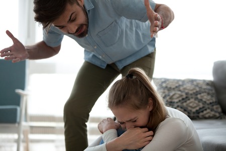 Unhappy crying frightened woman and aggressive man quarrelling at home. Angry husband emotionally arguing screaming shouting to scared wife psychological emotional abuse and domestic violence conceptの写真素材