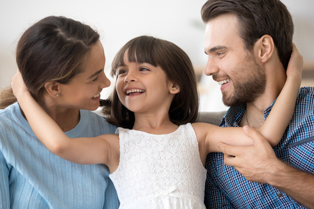 Portrait of multi-ethnic attractive mother father adorable little preschool daughter sitting together looking at each other embracing. New parents for adopted child or happy wellbeing family conceptの写真素材