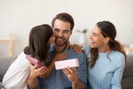 Head shot diverse family sitting embracing on couch at home. Little daughter kissing dad on cheek congratulate him at father day. Loving child make a gift for daddy at birthday. Life events conceptの写真素材