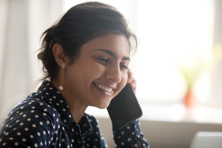Smiling beautiful millennial indian woman talking on the phone, happy young girl caller holding...
