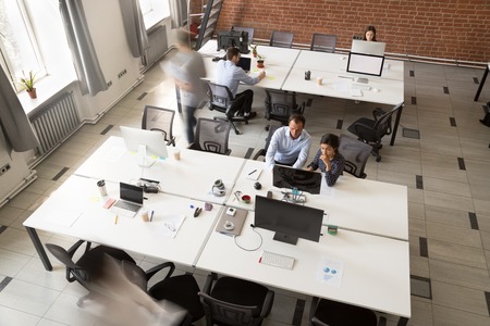 Modern coworking room interior with corporate team people group working on computers sitting at desks in open space, corporate staff workers colleagues using desktops, office rush concept, top viewの写真素材