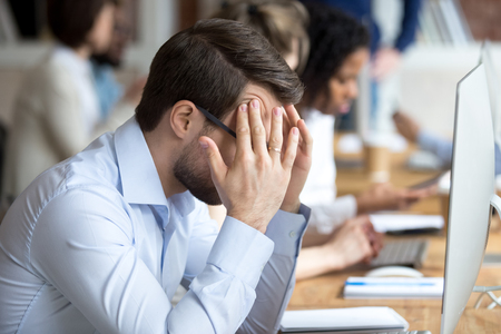Nervous male employee massage temples worry to finish work till deadline, stressed worker sit in front of computer suffering from headache or migraine, desperate man cope anxiety attack at workplaceの写真素材