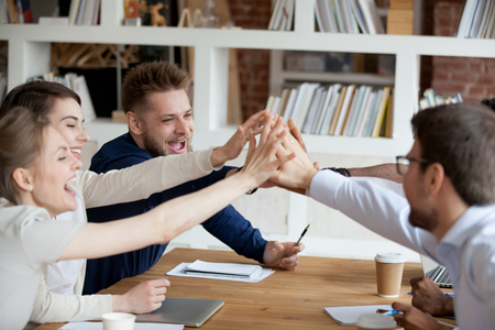 Excited millennial employees give high five celebrating shared win or team success, happy colleagues join hands involved in teambuilding activity at meeting, workers motivated for success show unityの写真素材