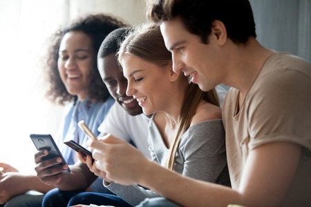Diverse people sitting in row, closeup focus on caucasian young female, friends having fun using...