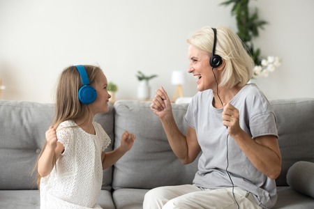 Happy senior grandmother and little kid granddaughter laughing listening to music in earphones...
