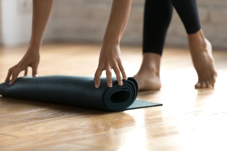 Close up woman hands unrolling mat preparing for fitness workout at gym studio. Sportive female folding rubber carpet after yoga session finishing sport training. Concept of active healthy lifestyleの写真素材