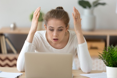 Upset young female looking at laptop screen shocked experience virus attack, frustrated girl read...