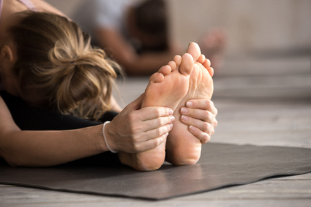 Yogi woman practicing yoga lesson, doing paschimottanasana exercise, Seated forward bend pose, working out, indoor close up. Feet therapy and sole treatment, well being, wellness conceptの写真素材