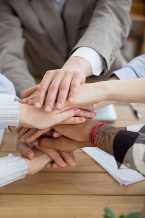Close up of multiracial workers join hands together in stack show support, reach shared goal, diverse people engaged in teambuilding activity or training at meeting, promise help. Cooperation conceptの写真素材