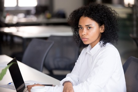 Focused young African American woman looking in distance at workplace, doubting female serious employee, student thinking of difficult job, question, task, received bad news, using laptopの写真素材