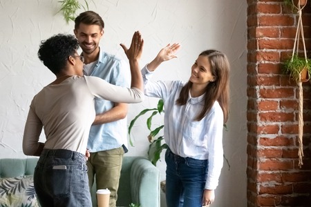 Happy African American woman giving high five with female friend, greeting, celebrating meeting in cafe, excited multiracial students or colleagues group in good friendly relationsの写真素材