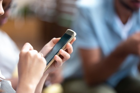 Young woman holding phone in hands, reading message, news, browsing internet, online mobile apps, using device at meeting, looking at screen, technology addiction, hands view close up