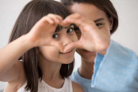 Portrait of little happy girl and mother join hands forming heart shape as concept of giving love, child mum connection unity, cute kid daughter and mom bonding looking at camera, child care adoptionの写真素材