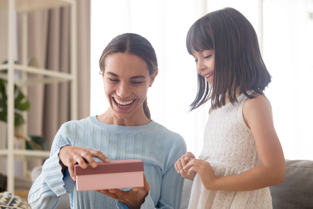 Excited cheerful mommy laughing opening gift box with present from child daughter, cute kid girl congratulating happy mom with birthday celebrating mothers day concept making funny surprise conceptの写真素材
