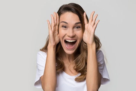 Excited young woman feeling amazed by unbelievable sale looking at camera screaming with joy isolated on white studio wall, funny euphoric girl winner on blank light background, head shot portraitの写真素材