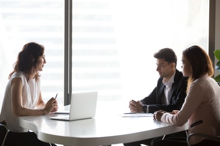 Diverse multi-ethnic business people communicating sitting at office meeting table, serious multiracial hr talking to applicant at job interview, recruitment, consulting and negotiations conceptの写真素材