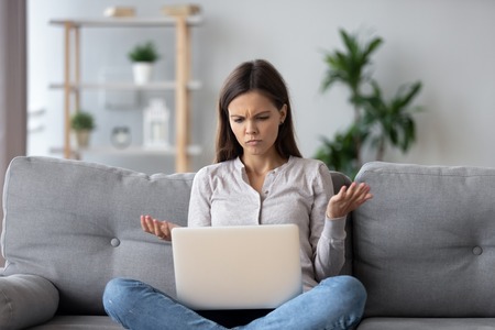 Confused young woman looking on laptop at home feeling bewildered by no connection, reading online news in internet, annoyed teen girl angry with stuck computer problem, scam spam email, system error