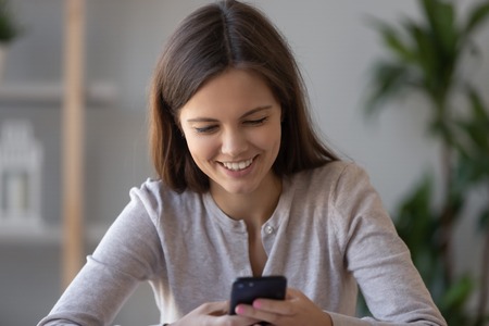 Happy teen girl using smartphone chatting in social media playing mobile game, smiling young woman user holding cellphone reading good news texting receiving message on phone, shopping in applicationの写真素材