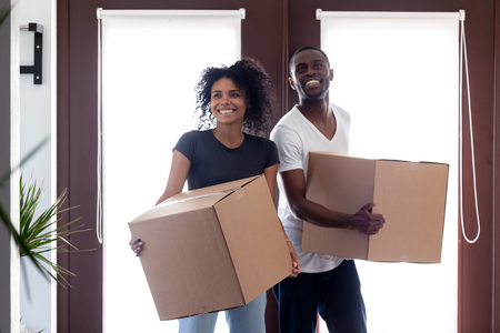 Excited black couple carry boxes entering big modern house on moving day, happy tenants african renters standing in hallway holding belongings looking around, welcome to new home, relocation conceptの写真素材