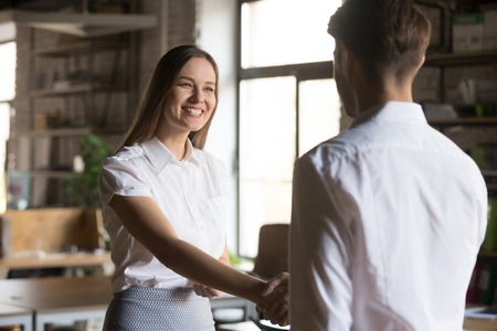 Back view of male employer or boss shake hand of excited female employee greeting with job promotion or employment, businessman handshake woman worker congratulating with work successの写真素材