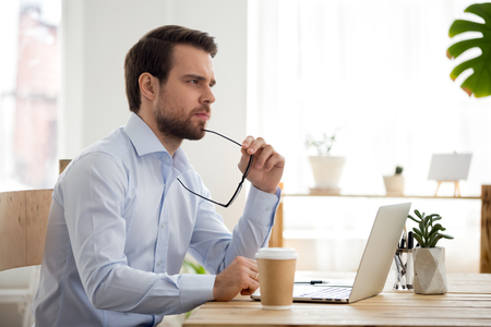 Thoughtful serious businessman lost in thoughts at work with laptop, focused executive thinking of problem solution, worried puzzled manager pondering question or solving business issues at workplaceの写真素材