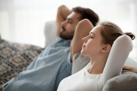Relaxed couple resting on comfortable couch, happy calm man and woman enjoying relaxation having nap on sofa breathing fresh air feeling relief, peace of mind on stress free day at home conceptの写真素材