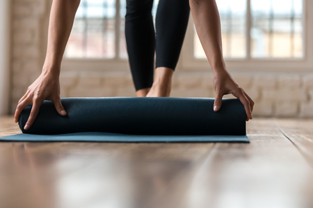Close up of sportive female wearing sportswear folding yoga mat after workout session in fitness studio, fit woman rolling pilates sport facilities after training in gym. Healthy lifestyle conceptの写真素材