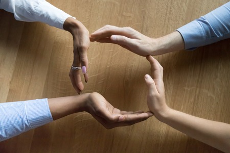 Above close up view four human hands businesswomen and businessman making a circle on wooden background, teammates join palms in shape of circle, protecting and showing care of their business conceptの写真素材