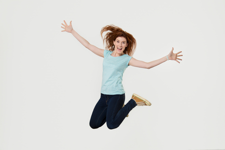 Happy active young woman jumping in air having fun screaming with joy isolated on white grey blank studio background, excited female winner feeling free celebrating success, full body length portraitの写真素材