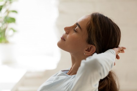 Close up side view female face with closed eyes putting hands behind head resting after busy fruitful working day. Student take a break relaxing feeling good having inner balance. No stress conceptの写真素材